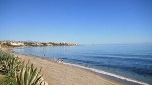 Ein Strand mit klarem, blauem Wasser, einem sandigen Ufer und einigen Spaziergängern.