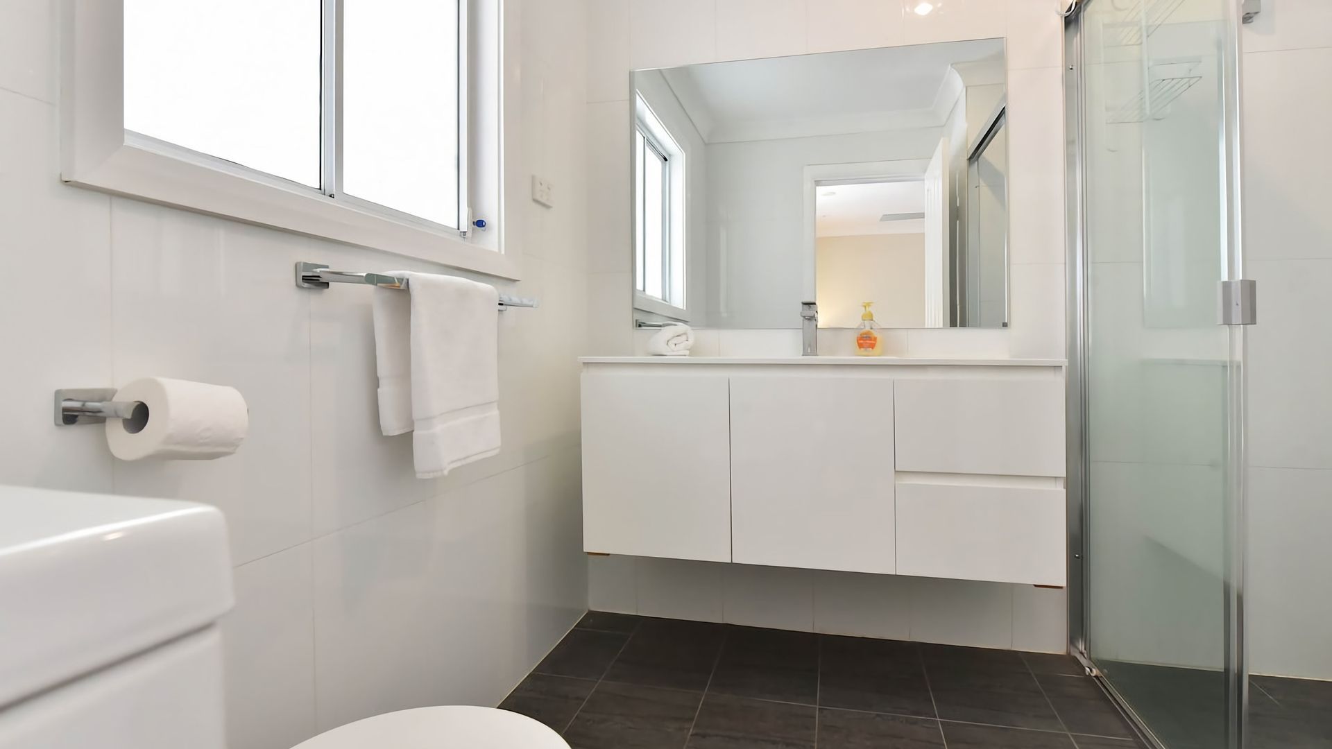 A modern bathroom with a toilet, a towel rack, a mirror, and a shower.