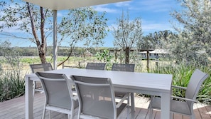 Eine Terrasse im Freien mit einem weißen Tisch und Stühlen, umgeben von Pflanzen und Bäumen.