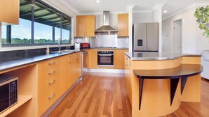 A modern kitchen with wooden cabinets, a built-in oven, and a large window overlooking greenery.