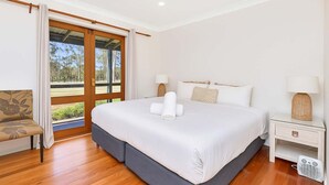 A spacious bedroom with a large bed, a chair, a bedside table with a lamp, and a view through a glass door to an outdoor area.