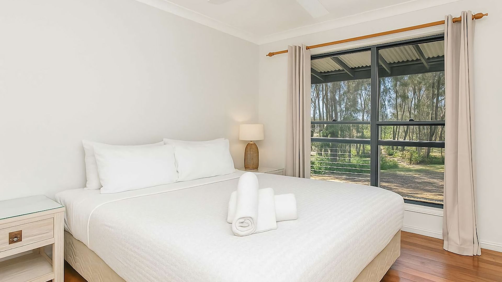 A hotel room with a large bed, a bedside table, a lamp, and a window with curtains.
