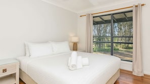 A hotel room with a large bed, a bedside table, a lamp, and a window with curtains.
