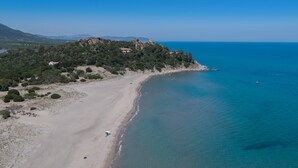 Paesaggio costiero con spiaggia, una torre su una collina e montagne in lontananza.
