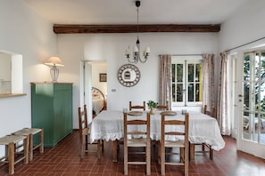 Uma sala de jantar com mesa posta para quatro pessoas, cadeiras de madeira, um lustre e um armário verde.