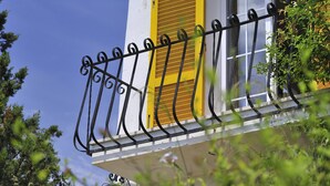 Un balcone con persiane gialle, una finestra e un parapetto in ferro battuto nero.