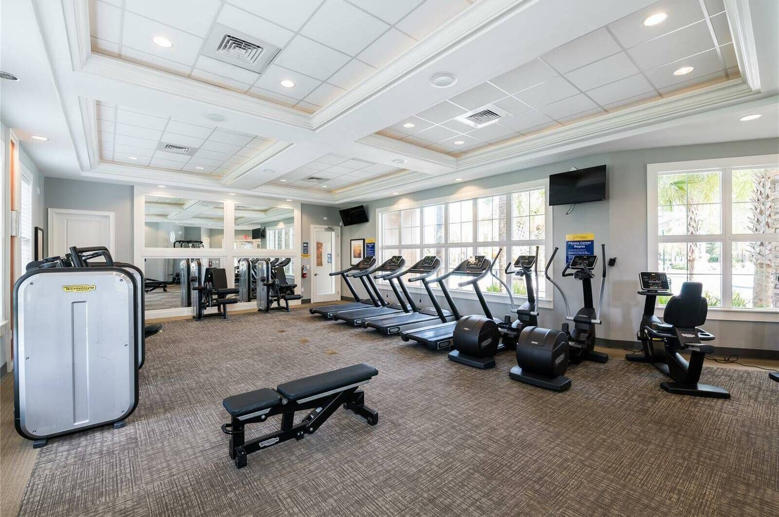 A gym with treadmills, elliptical machines, and a bench.