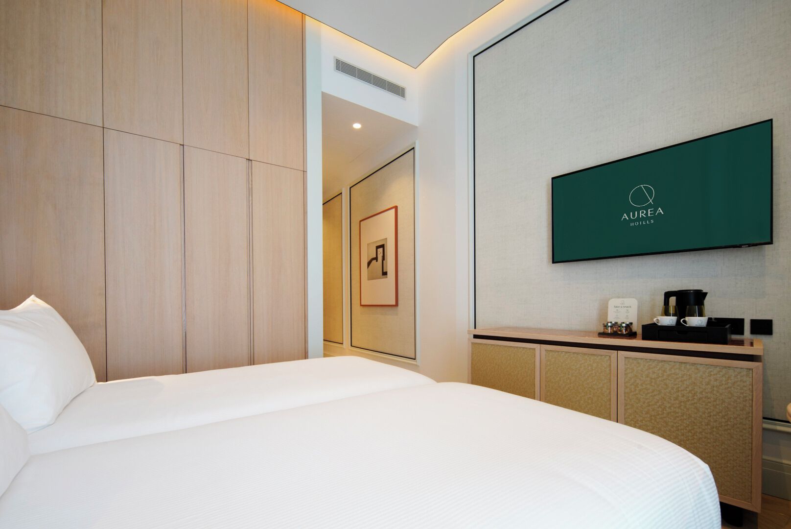 Ein Hotelzimmer mit Bett, einer Kaffeestation und einem Fernseher, der den Namen des Hotels zeigt.