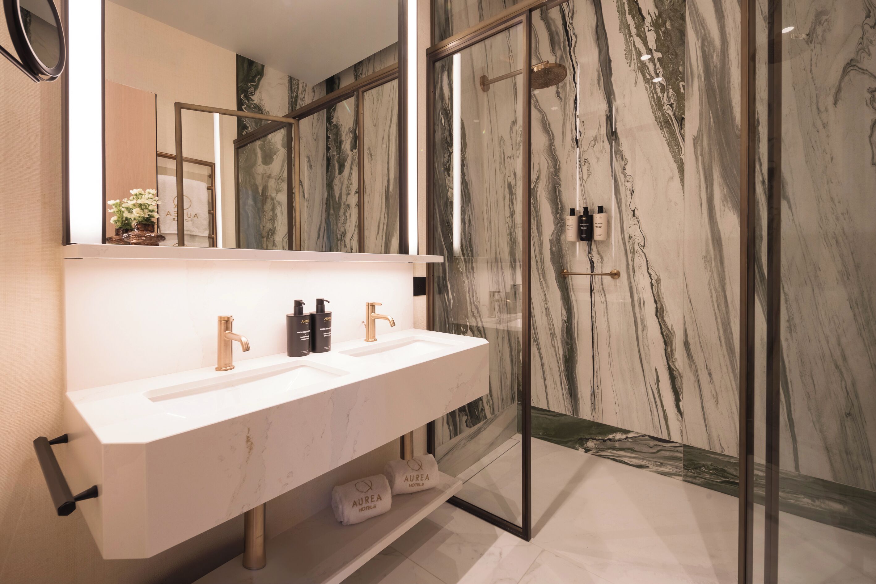 Un baño moderno con lavamanos de mármol blanco, dos grifos y una ducha con cerramiento de vidrio.