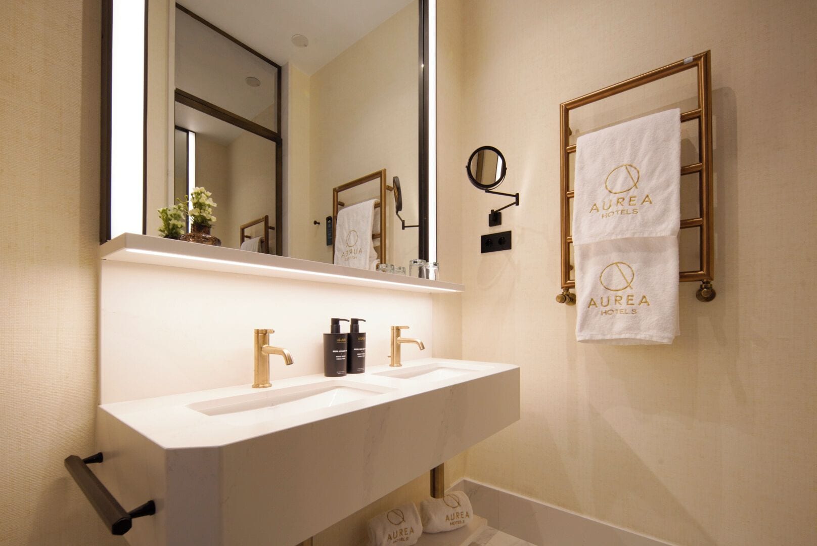 Un baño con un lavabo blanco, grifos dorados, un espejo grande y dos toallas colgadas en un perchero.