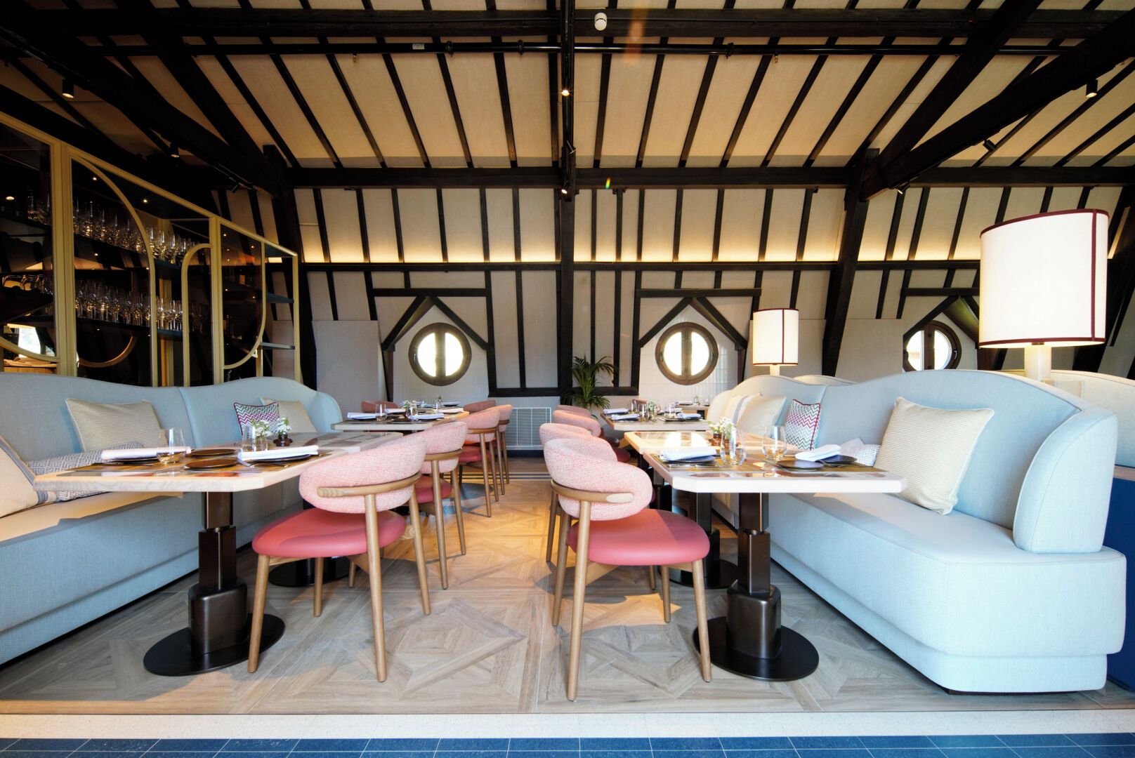A modern dining area with round tables, cushioned seating, and a high ceiling with exposed beams.