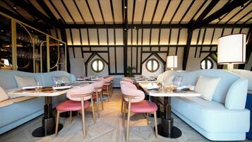 A modern dining area with round tables, cushioned seating, and a high ceiling with exposed beams.