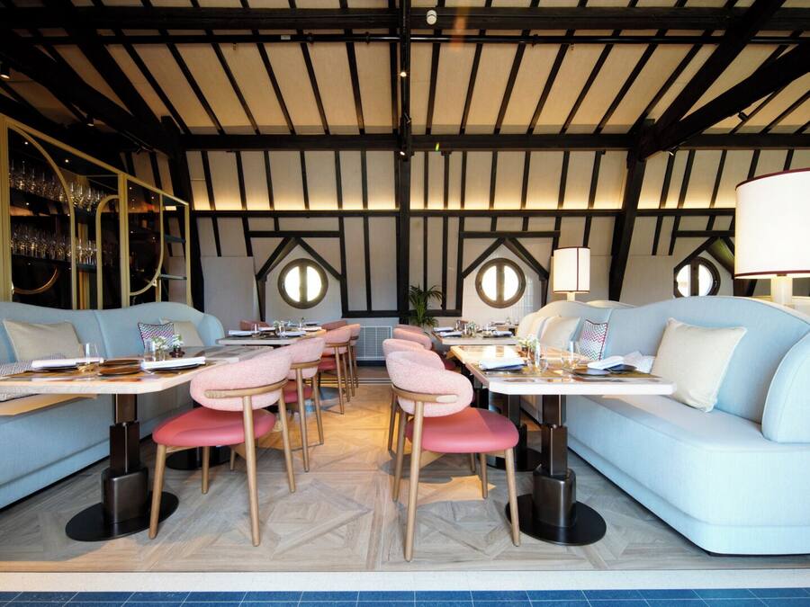 A modern dining area with round tables, cushioned seating, and a high ceiling with exposed beams.