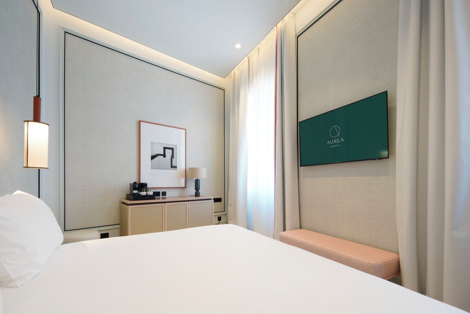 Una habitación de hotel con una cama grande, un escritorio con lámpara, un cuadro enmarco y un televisor mostrando el nombre del hotel.