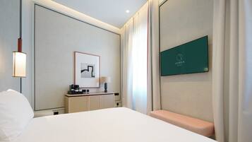 Una habitación de hotel con una cama grande, un escritorio con lámpara, un cuadro enmarco y un televisor mostrando el nombre del hotel.