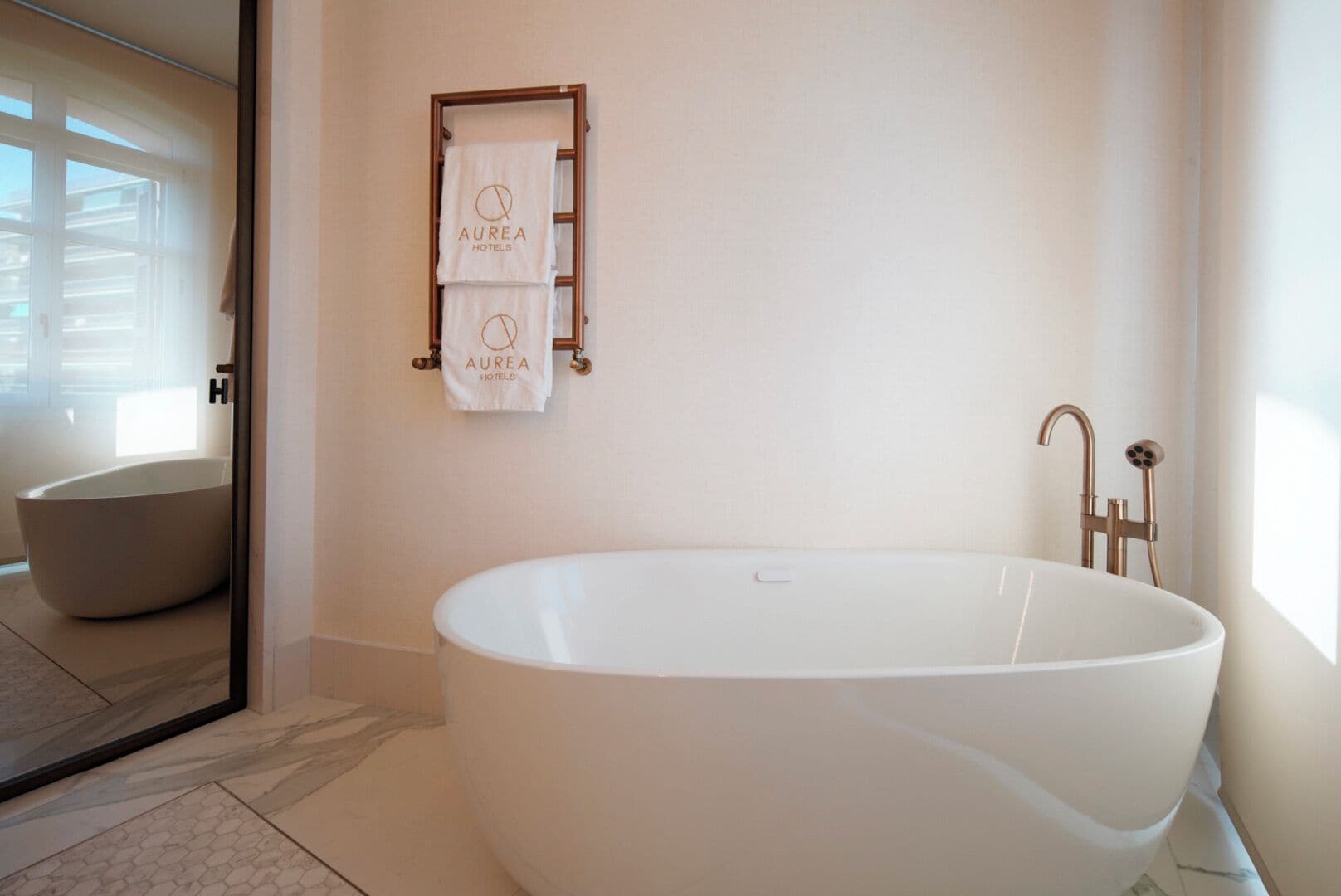 A modern bathroom with a freestanding bathtub, a towel rack with branded towels, and a large mirror.