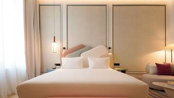 A hotel room with a large bed, bedside tables, a nightstand, a lamp, and a sofa.