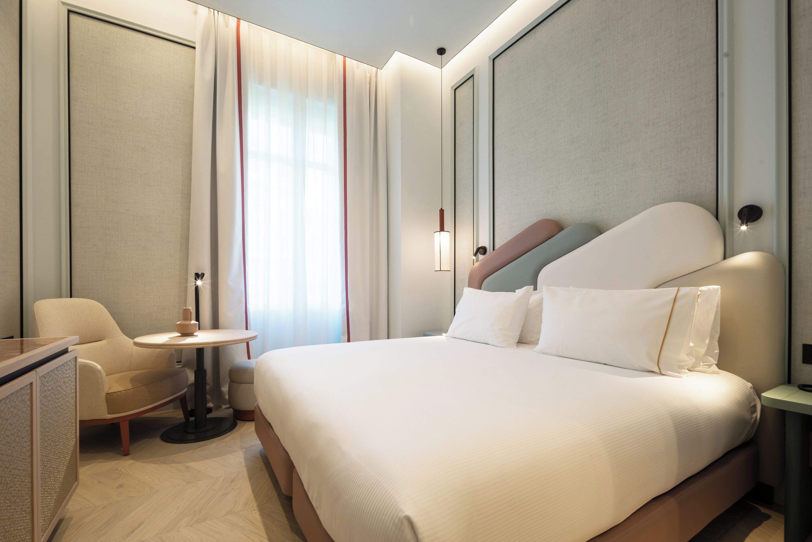 A hotel room with a bed, a desk, a chair, a small table, and a window with curtains.