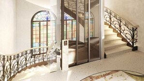 En storslagen trappa med utsmyckade metallräcken, en glashiss och ett runt marmorgolv.