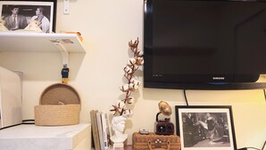 Una scrivania ordinata con una televisione, libri, un cesto decorativo e un vaso con fiori secchi.