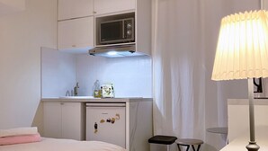 Una camera da letto con un letto, una scrivania, un forno a microonde, un cestino e una lampada.