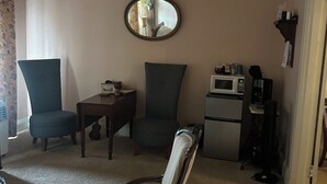 Een woonkamer met een ronde spiegel, twee stoelen, een salontafel, een magnetron en een koelkast.