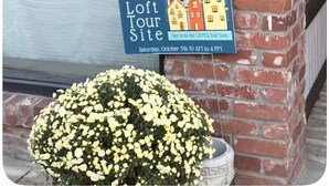 Een bord voor een rondleiding door een loft, met datum en tijd, en een pot met gele bloemen.