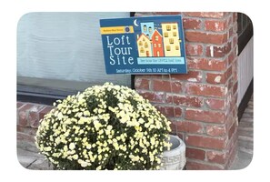 Une pancarte indiquant le lieu d’une visite guidée d’un loft, avec la date et l’heure, et un pot de fleurs contenant des fleurs jaunes.