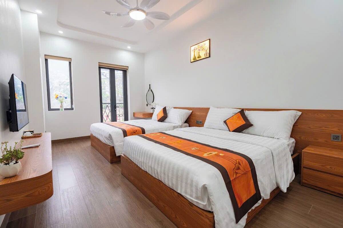 A hotel room with two beds, a wooden nightstand, a TV, and a ceiling fan.