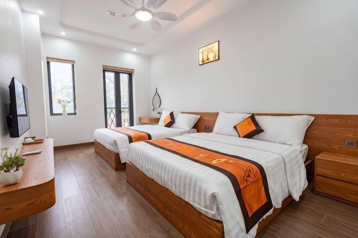 A hotel room with two beds, a desk, a TV, and a window.