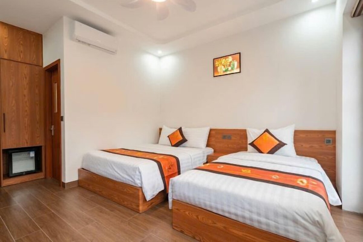 A hotel room with two beds, wooden headboards, a ceiling fan, an air conditioning unit, and a small television.