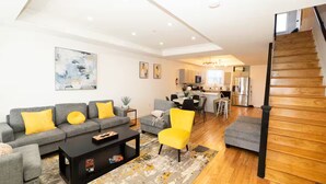 A modern living room with a grey sofa, yellow cushions, a black coffee table, and a wooden staircase. - 7 bdrm 7 bth 3 kitchens NW DC w/parking & balcony (Washington)
