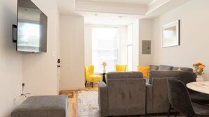 A modern living room with a grey sectional sofa, a yellow armchair, and a dining area with a round table. - 7 bdrm 7 bth 3 kitchens NW DC w/parking & balcony (Washington)