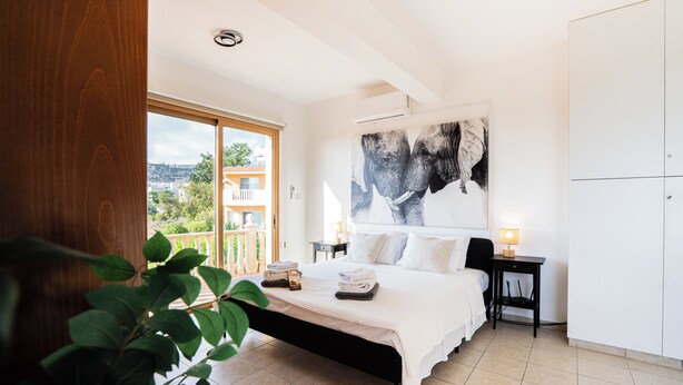 Una camera da letto con un letto, un comodino, una lampada, un'ampia finestra e vista sugli edifici.