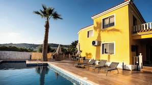 Una villa gialla con piscina, mobili da esterno e vista sul paesaggio.