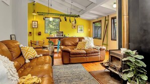 A living room with a yellow wall, brown leather sofas, a coffee table, and a fireplace. - Treetop Sanctuary Serene Cottage near Mount Lofty (Crafers West)