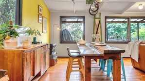A cozy dining area with a wooden table, chairs, and a bar counter. There are large windows providing views of the outdoors. - Treetop Sanctuary Serene Cottage near Mount Lofty (Crafers West)