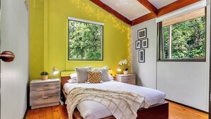 A bedroom with a bed, bedside tables, a lamp, and a window with a view of greenery. - Treetop Sanctuary Serene Cottage near Mount Lofty (Crafers West)
