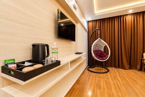 A hotel room with a wooden floor, a black coffee maker, a water bottle, a hanging chair, and a flat-screen TV mounted on the wall. - Priya Residency Pondicherry (Vanur)
