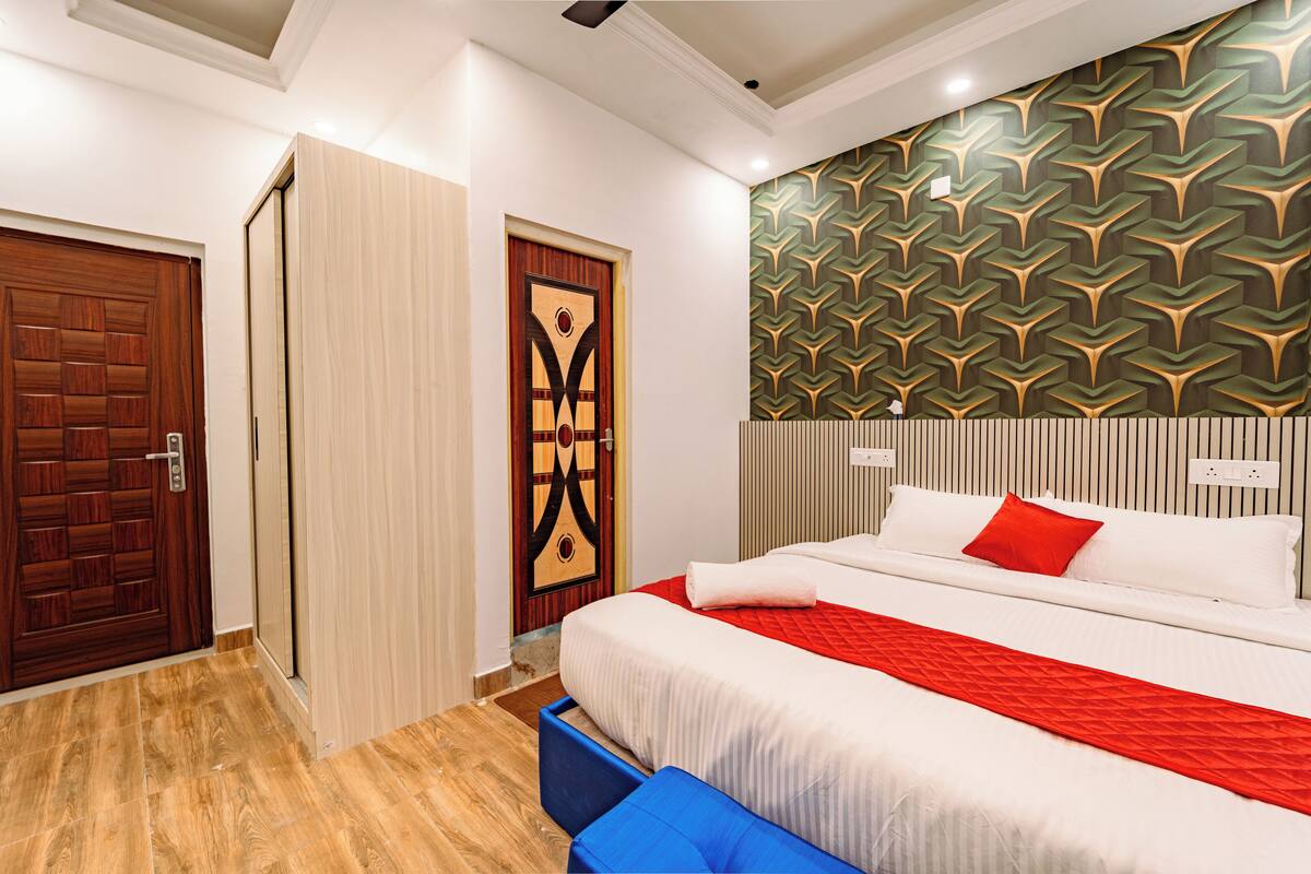 Una habitación de hotel con cama, una colcha roja y blanca, un banco azul y un papel tapiz estampado.