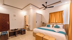 A modern hotel room with a large bed, a ceiling fan, a wooden bench, and a small table. - Priya Residency Pondicherry (Vanur)