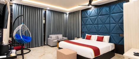 A modern hotel room with a large bed, a hanging chair, a sofa, a desk, and a ceiling fan.
