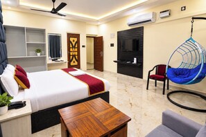 A hotel room with a bed, a desk, a hanging chair, a TV, and an air conditioning unit. - Priya Residency Pondicherry (Vanur)