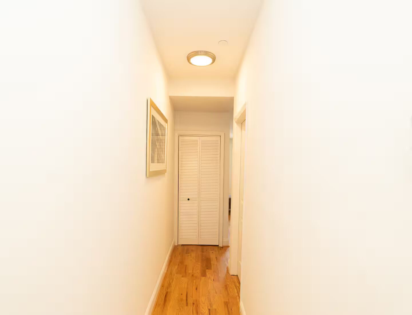 A narrow hallway with wooden flooring, white walls, and a door at the end.