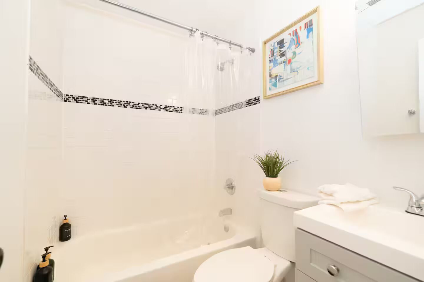 Un baño con ducha, inodoro, lavamanos y un cuadro en la pared.