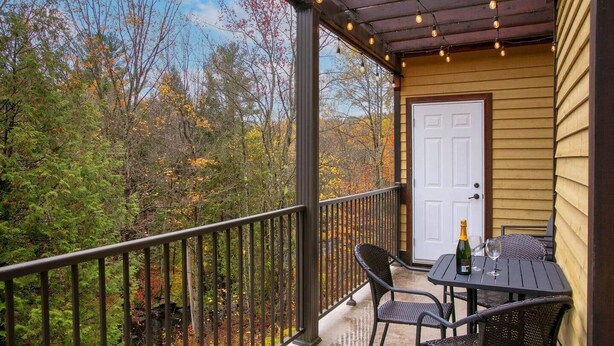 A covered outdoor area with a table and chairs, a door, and a view of trees. - Hôtel à la maison - Entre Mont et rivière (Orford)