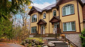 A two-story house with a stone foundation, a front porch, and a driveway leading to the entrance. - Hôtel à la maison - Entre Mont et rivière (Orford)