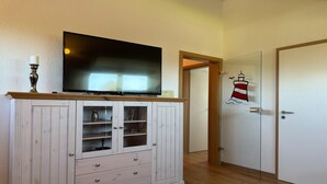 Ein Zimmer mit Fernseher auf einer Holzkommode, einer Tür mit Leuchtturm-Aufkleber und einer weißen Tür.