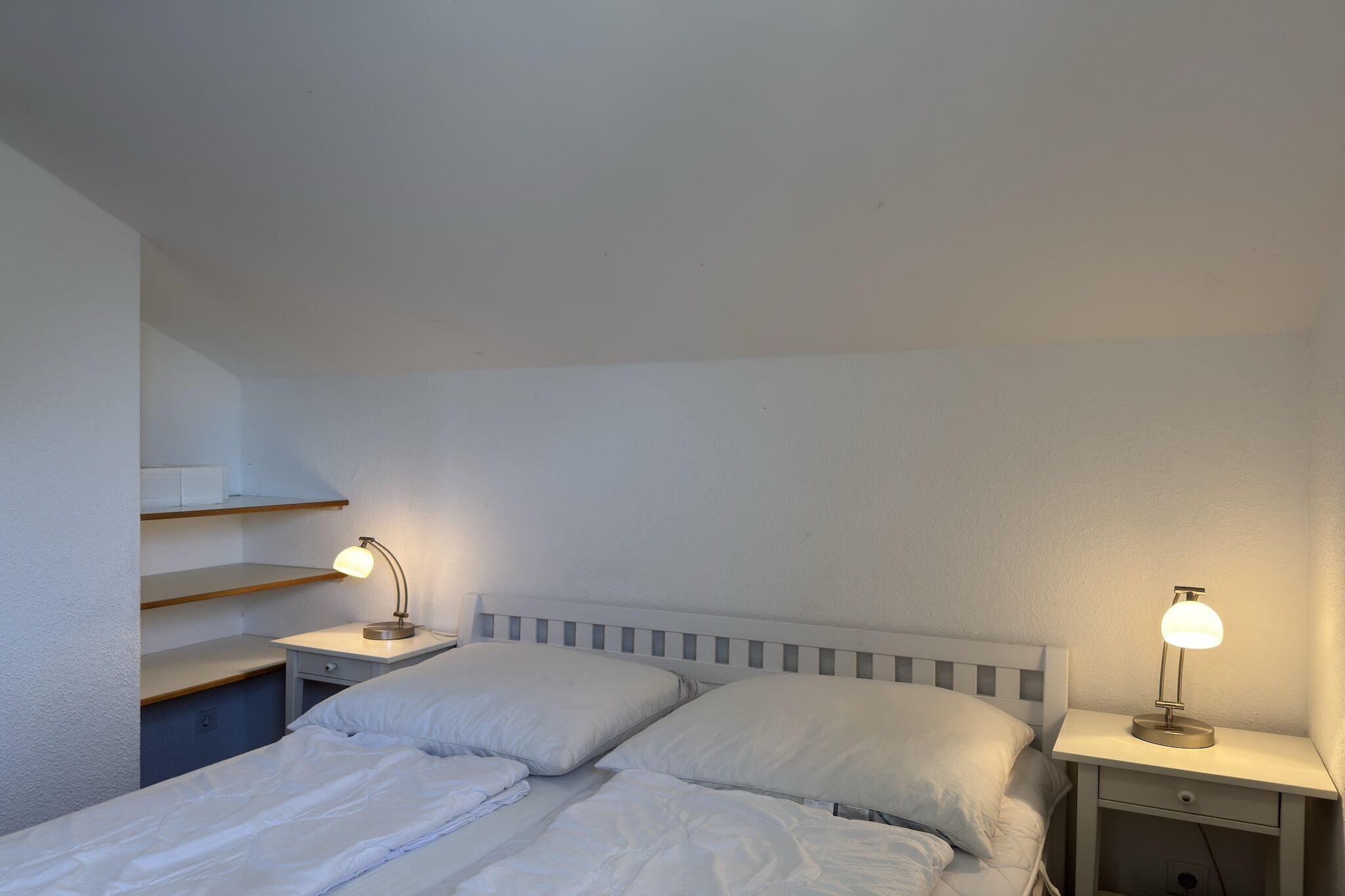 A bedroom with a bed, two bedside tables, and a nightstand with a lamp.