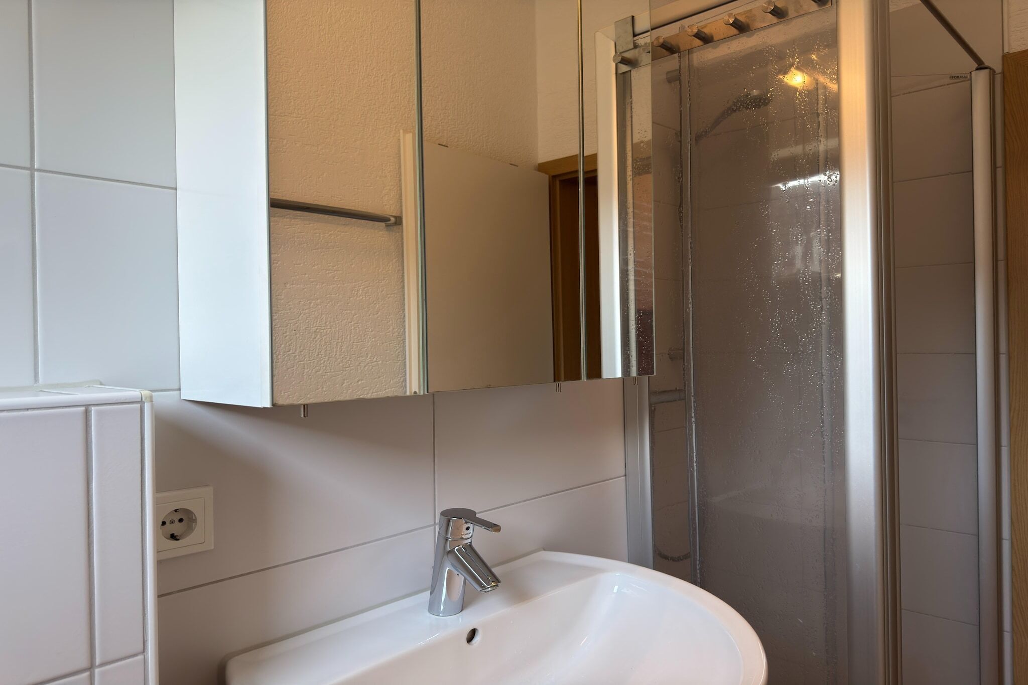 Ein Badezimmer mit einem weißen Waschbecken, einem Spiegel, einer Duschkabine und einem Handtuchhalter.